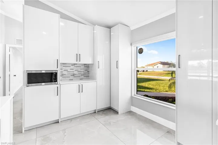 Kitchen with tasteful backsplash, stainless steel microwave, ornamental molding, and white cabinets