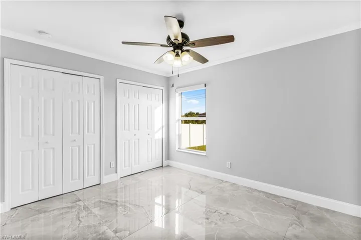 Unfurnished bedroom with ceiling fan, multiple closets, and crown molding