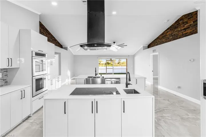 Kitchen featuring lofted ceiling, a center island with sink, white cabinets, sink, and appliances with stainless steel finishes