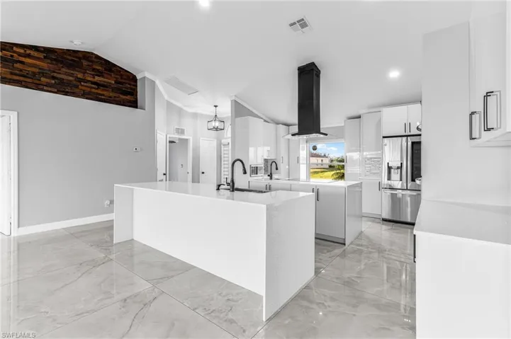 Kitchen with vaulted ceiling, stainless steel refrigerator with ice dispenser, sink, ventilation hood, and a kitchen island