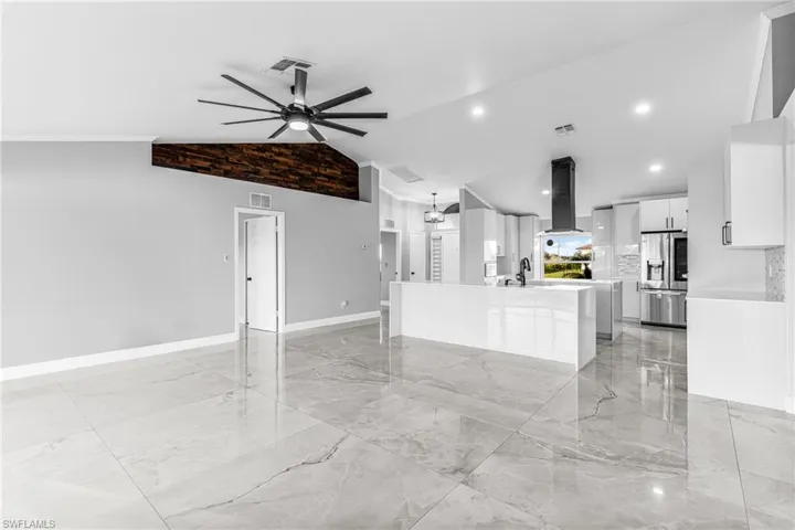 Kitchen featuring stainless steel fridge, exhaust hood, an island with sink, white cabinets, and lofted ceiling