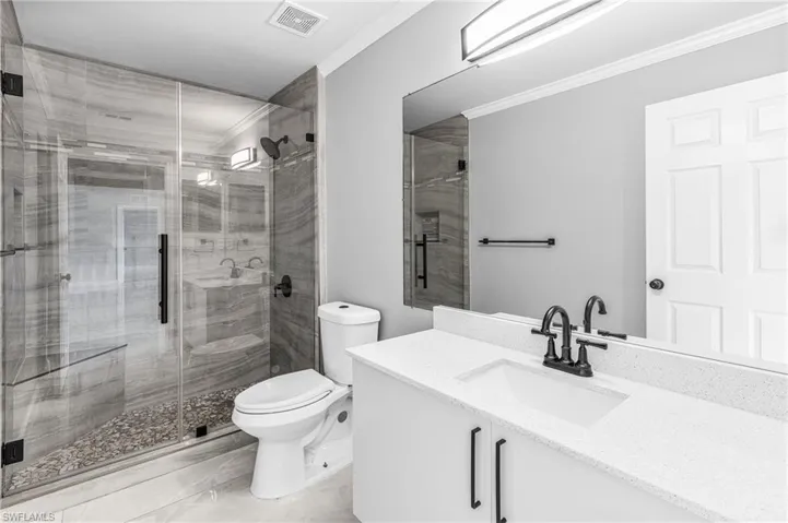 Bathroom featuring toilet, vanity, crown molding, and a shower with shower door