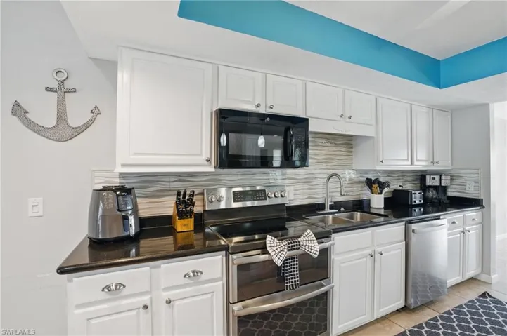 Kitchen featuring decorative backsplash, stainless steel appliances, white cabinets, and a sink