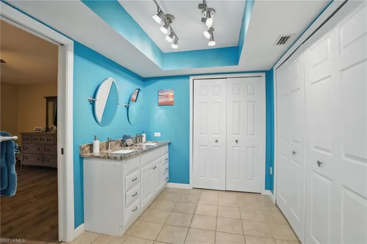 Bathroom with a raised ceiling, double vanity, visible vents, a closet, and baseboards