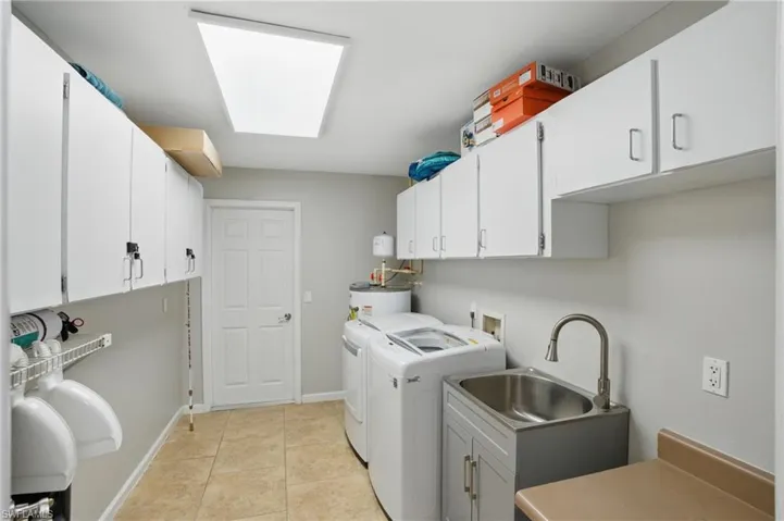 Clothes washing area featuring washer and clothes dryer, a sink, water heater, cabinet space, and baseboards