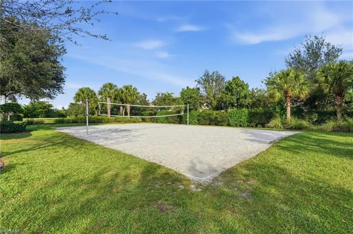 Sand volleyball court featuring a net and lush green perimeter