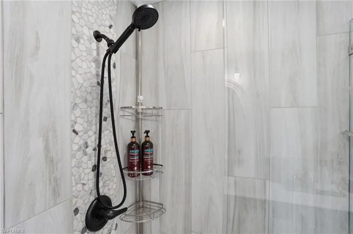 Shower featuring large format wood-grain tile, a pebble mosaic accent strip, and matte black fixtures