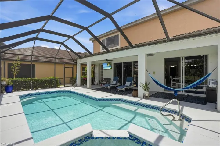 Screen-enclosed pool area featuring a rectangular swimming pool with integrated steps, a tiled spa, and a white concrete deck