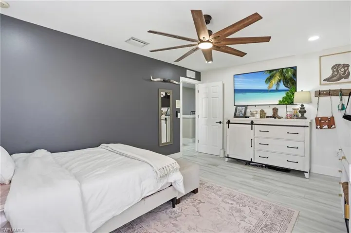 Spacious room featuring light wood-finish flooring, a contemporary ceiling fan with integrated lighting, recessed lighting, and a white six-drawer dresser with a barn door accent