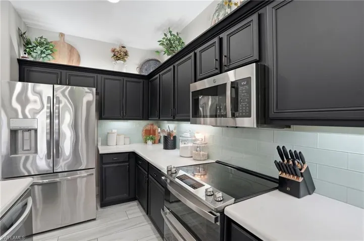 Kitchen featuring dark cabinetry, stainless steel appliances, light countertops, and a subway tile backsplash