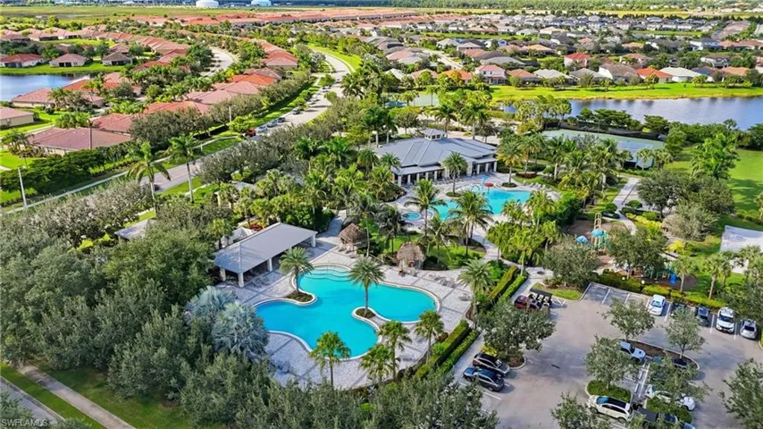 Expansive community recreation area featuring multiple swimming pools, substantial club building, numerous mature palm trees, and nearby residential homes