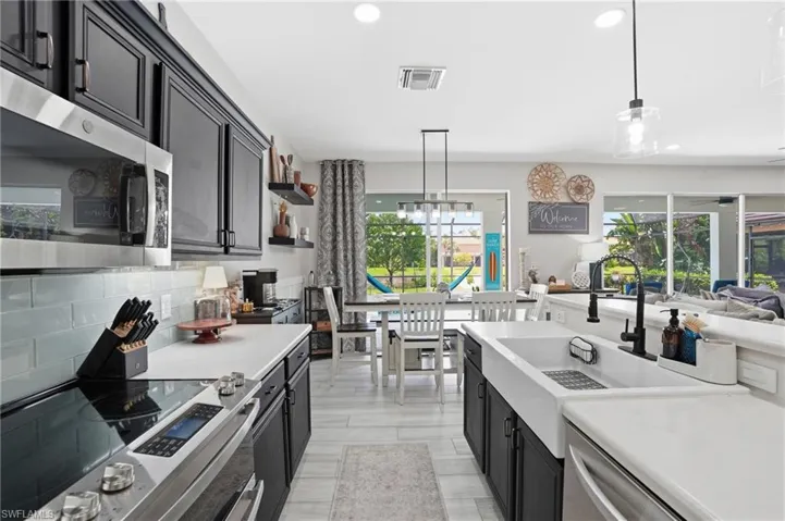 Modern kitchen featuring dark cabinetry, white countertops, stainless steel appliances, a white farmhouse sink, and light wood-finish flooring