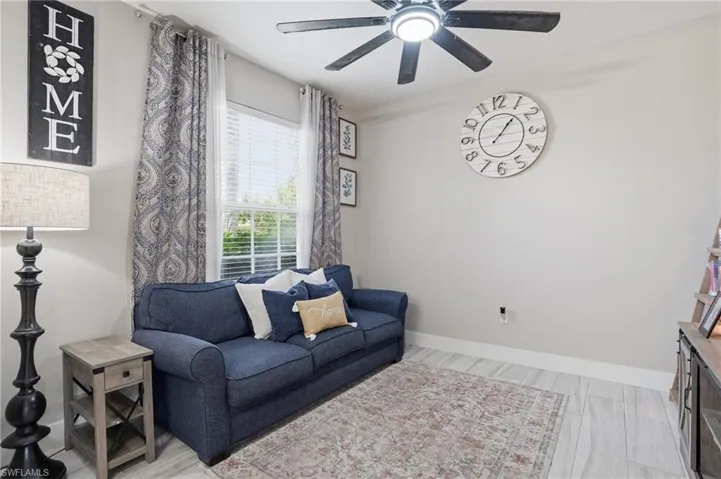 Bright room featuring a ceiling fan with integrated lighting, light-toned wood-finish flooring, a window with blinds and patterned curtains, and a neutral wall color