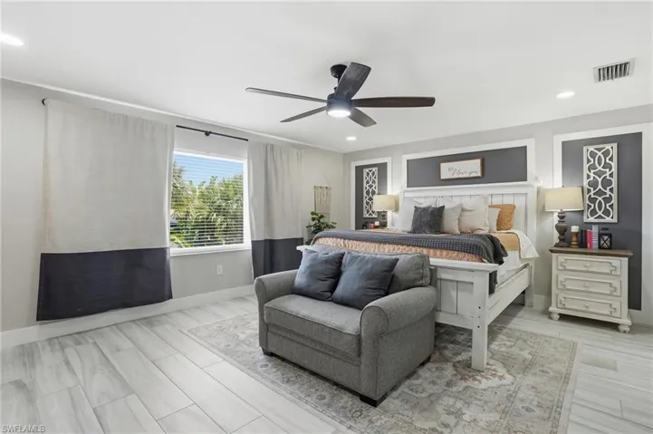 Spacious bedroom featuring wood-finish flooring, a contemporary ceiling fan with integrated lighting, recessed lighting, a large window with blinds, and decorative wall paneling