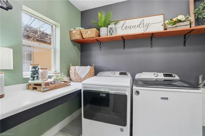 Dedicated laundry area featuring a built-in countertop, window, and wood shelving with black metal brackets