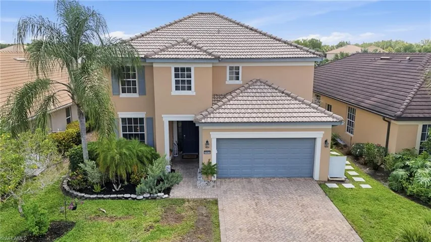 Two-story stucco residence featuring a tiled roof, paver driveway, and an integrated garage