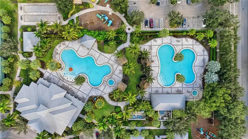 Aerial perspective showcasing two distinct swimming pools, each surrounded by extensive paver decking and lush tropical landscaping