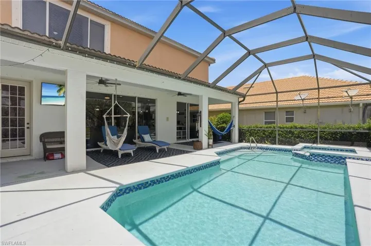 Screen-enclosed pool area with a covered patio, featuring an inground swimming pool with blue mosaic tile accents, an integrated spa, and an attached covered lanai with ceiling fans