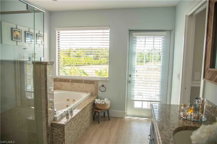 Bathroom with wood finished floors, a jetted tub, a stall shower, and double vanity
