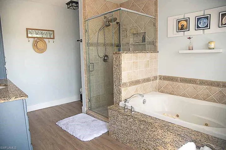 Full bathroom featuring a stall shower, a jetted tub, wood finished floors, and vanity