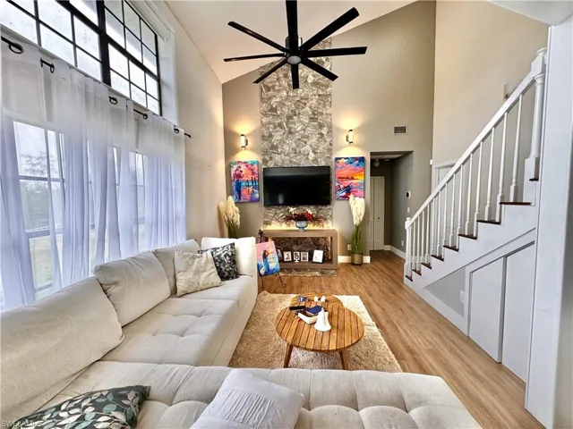 Living room with high vaulted ceiling, light wood-style floors, ceiling fan, and stairway