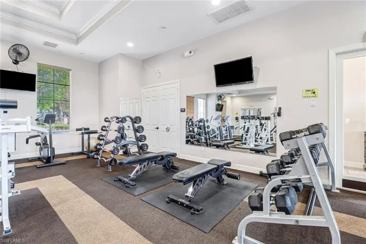 Dedicated fitness space featuring tray ceilings, a large window with blinds, wall-mounted televisions, mirrored walls, and durable flooring
