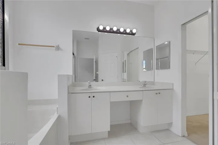 Double vanity with individual sinks, white cabinetry, integrated makeup area, and a large wall-mounted mirror