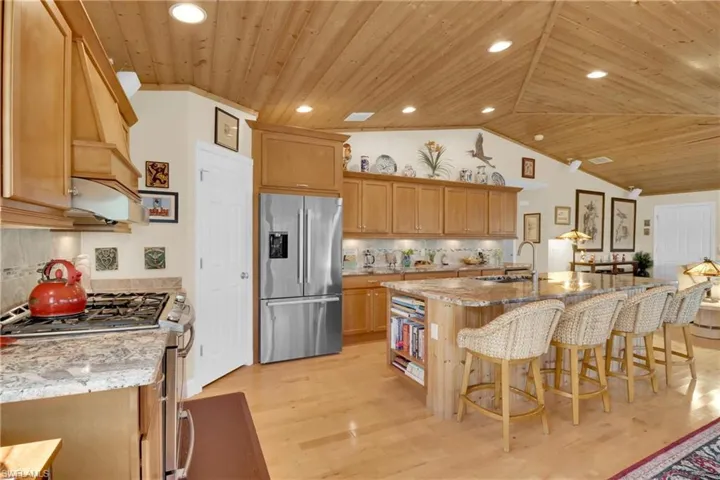 Kitchen with wooden ceiling, stainless steel appliances, vaulted ceiling, light stone countertops, and a breakfast bar area