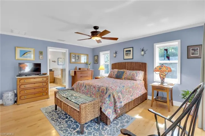 Bedroom with ornamental molding, multiple windows, light wood finished floors, ceiling fan, and ensuite bath