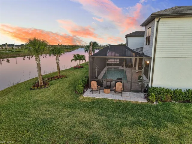 View of green lawn featuring a sunroom, a lanai, a patio, a water view, and an outdoor pool