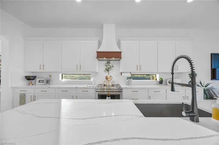 Kitchen featuring white cabinetry, high end range, light stone countertops, recessed lighting, and decorative backsplash