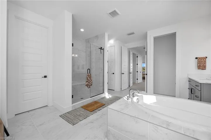 Bathroom featuring a marble finish shower, light marble finish flooring, vanity, and a bath