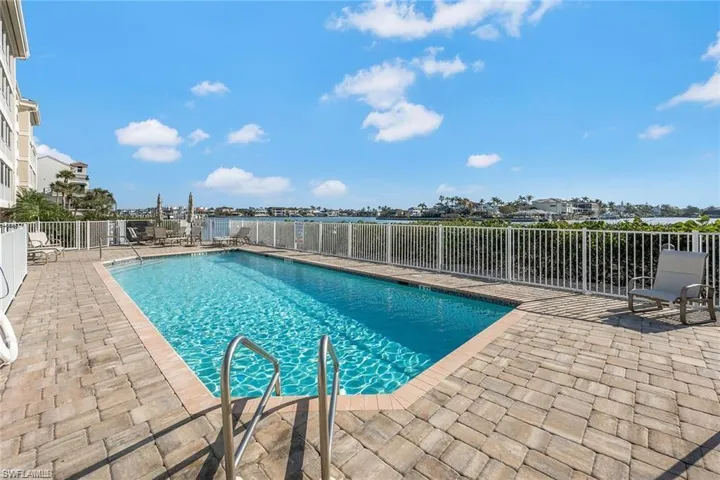 Swimming pool with paver decking, white perimeter fencing, and water frontage