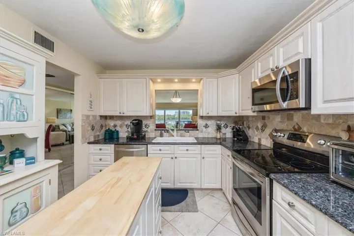 Kitchen with appliances with stainless steel finishes, light tile patterned floors, butcher block counters, and backsplash