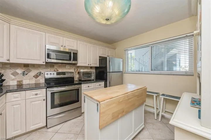 Kitchen featuring stainless steel appliances, decorative backsplash, light tile patterned floors, and dark stone counters