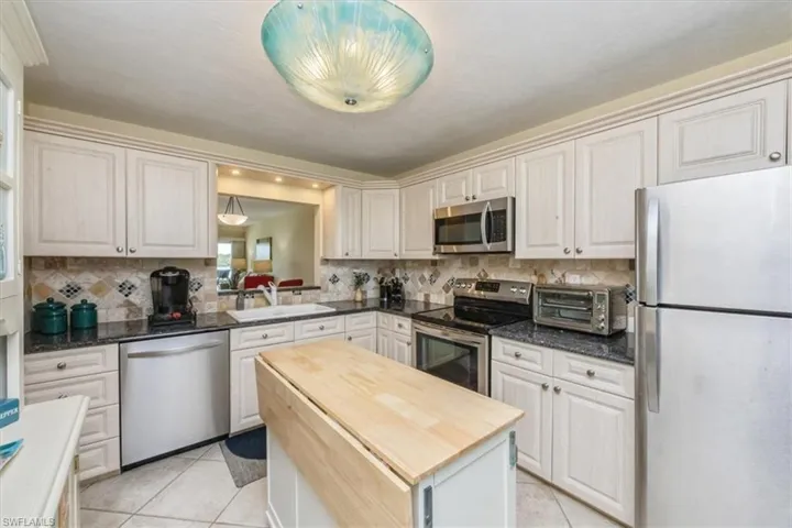 Kitchen with stainless steel appliances, light tile patterned floors, dark stone countertops, and backsplash