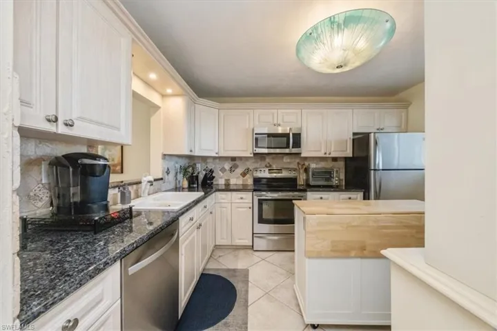 Kitchen with decorative backsplash, appliances with stainless steel finishes, light tile patterned flooring, dark stone countertops, and recessed lighting