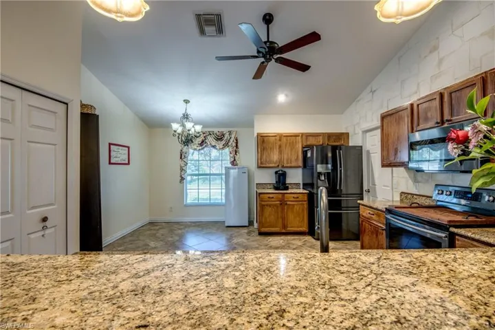Kitchen featuring stainless steel appliances, vaulted ceiling, brown cabinetry, a chandelier, and ceiling fan