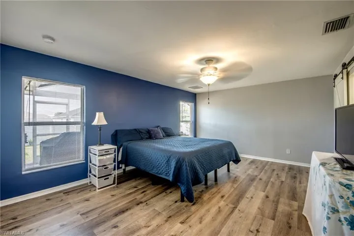 Bedroom with a barn door, light wood-style floors, baseboards, and ceiling fan