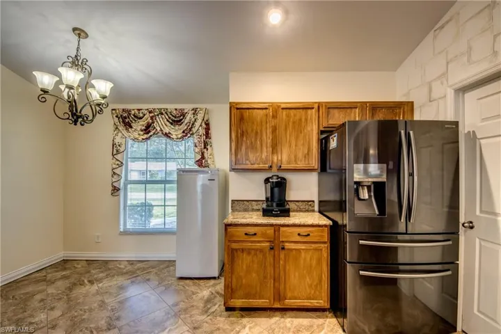 Kitchen featuring stainless steel fridge, fridge, brown cabinets, a chandelier, and light stone counters