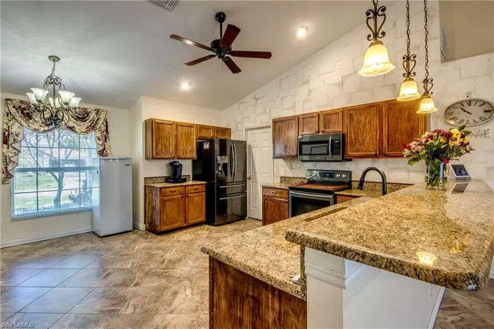 Kitchen featuring stainless steel appliances, brown cabinets, a peninsula, a ceiling fan, and a chandelier
