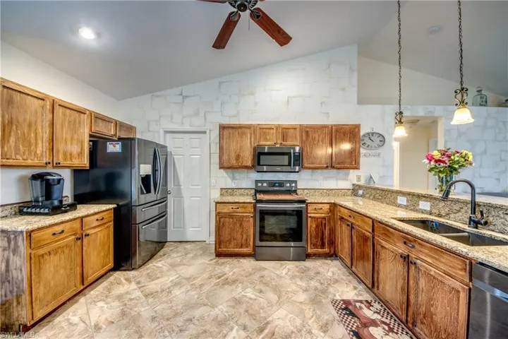 Kitchen featuring appliances with stainless steel finishes, a sink, lofted ceiling, ceiling fan, and brown cabinets