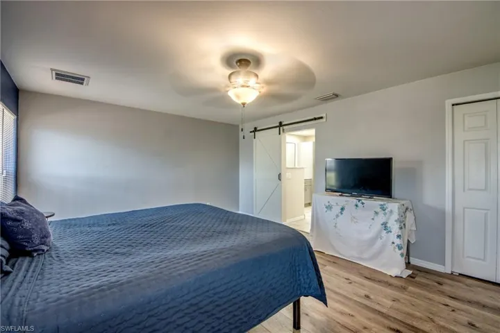 Bedroom with a barn door, light wood-style flooring, baseboards, and a ceiling fan