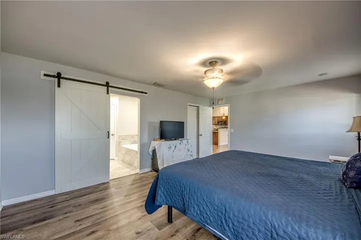 Bedroom with a barn door, wood finished floors, connected bathroom, baseboards, and ceiling fan