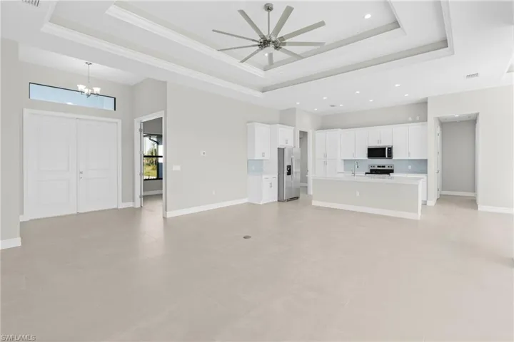 Unfurnished living room featuring a raised ceiling, a chandelier, and ceiling fan