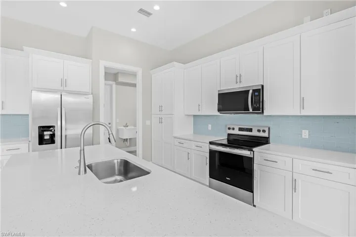 Kitchen with appliances with stainless steel finishes, backsplash, white cabinetry, light stone counters, and recessed lighting
