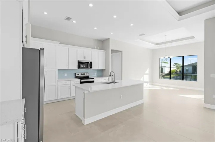 Kitchen with decorative backsplash, appliances with stainless steel finishes, a raised ceiling, white cabinetry, and recessed lighting