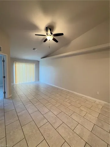 Tiled spare room featuring vaulted ceiling and ceiling fan