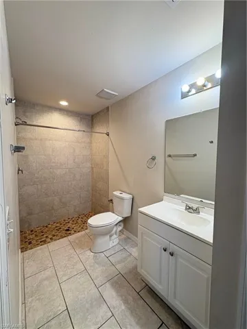 Bathroom with tiled shower, vanity, tile patterned floors, and toilet