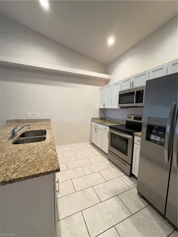 Kitchen featuring white cabinets, range, sink, stone countertops, and fridge